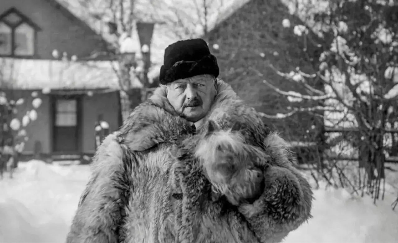 En man i päls och hatt, en av Anders Zorns fotografier, står i snö.