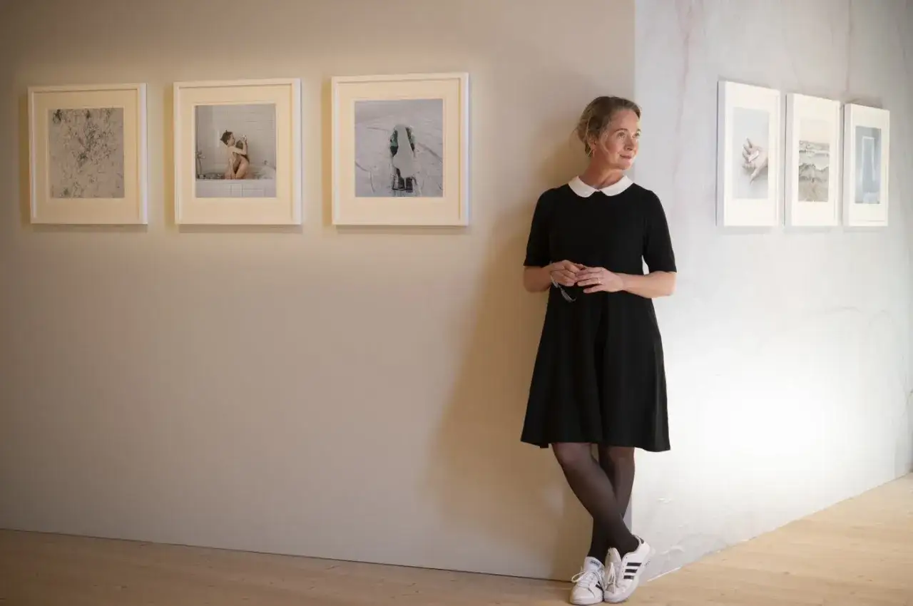 Anna Claren st&aring;r vid en v&auml;gg med konstverk. Hon b&auml;r en svart kl&auml;nning och tittar bort.