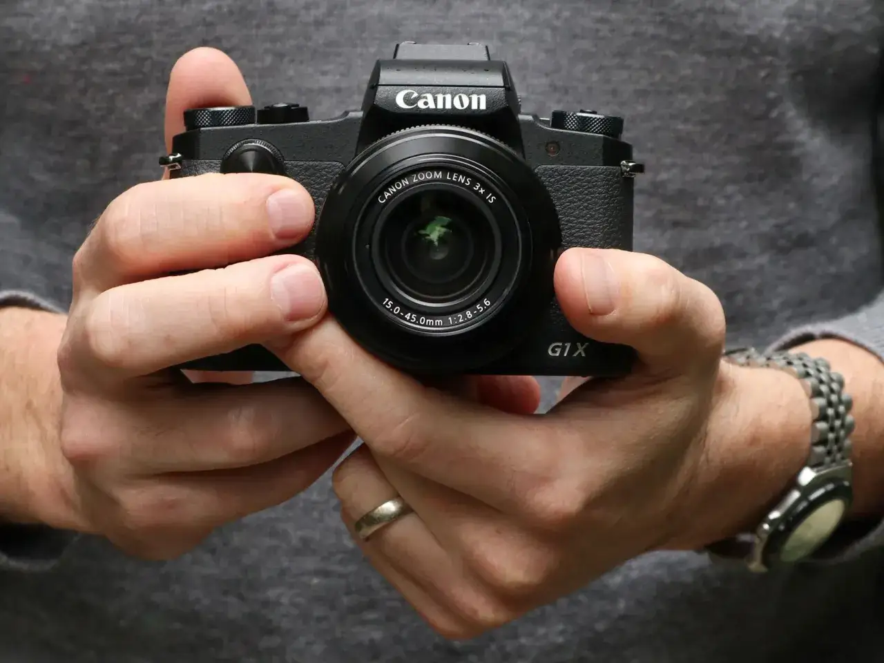 H&auml;nder h&aring;ller en Canon G1X Mark III kamera. En klocka syns p&aring; handleden.