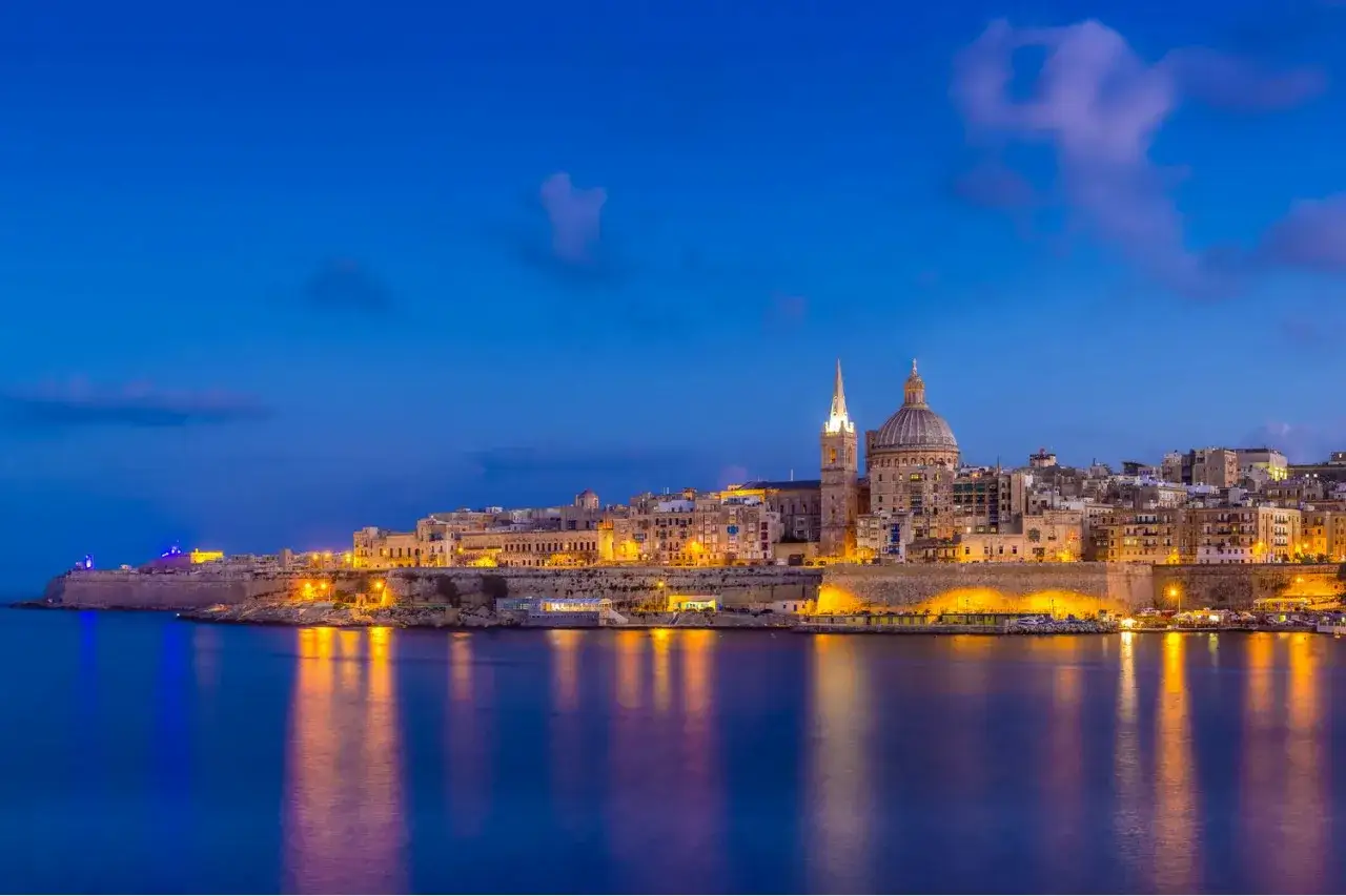 Valletta, Malta, badar i det magiska ljuset under blå timmen. Staden vaknar till liv med upplysta byggnader och reflekteras i det lugna vattnet.