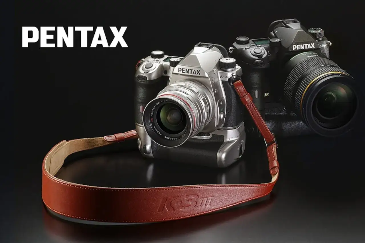 Tv&aring; Pentax K3 kameror, en silverf&auml;rgad och en svart, med en brun l&auml;derrem med pr&auml;glad text.
