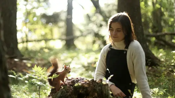 En ung kvinna, Dani Connor, sitter i skogen och tittar på en ekorre som sitter på en stubbe.