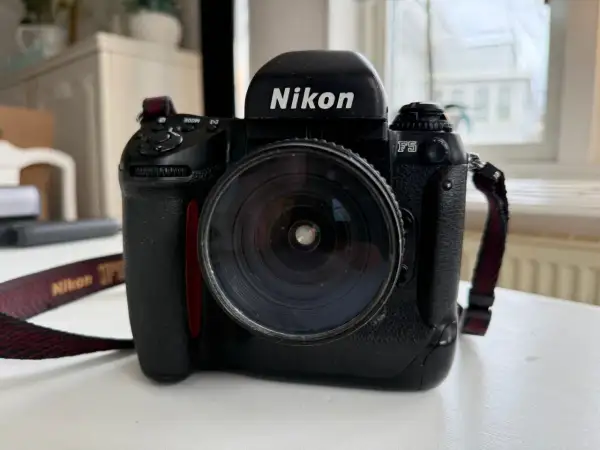 En svart Nikon F5 systemkamera med ett stort objektiv. Kameraremmen med texten "Nikon" syns.