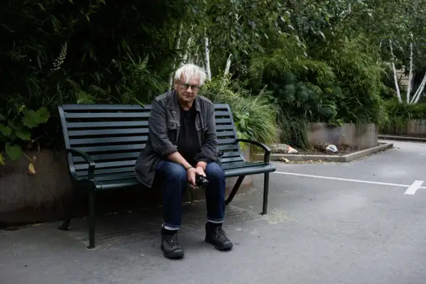 Anders Petersen sitter på en parkbänk, omgiven av grönska.