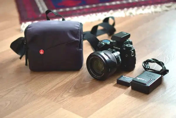 En Fujifilm XH1-kamera med objektiv, batteri, laddare och väska ligger på ett trägolv.