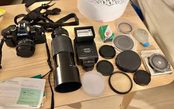 En Canon AE-1 kamera med objektiv, blixt, film och tillbehör ligger på ett träbord.