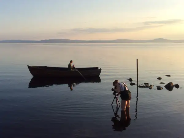 Nygårds Karin Bengtsson filmar en person i en roddbåt vid solnedgången på en lugn sjö.