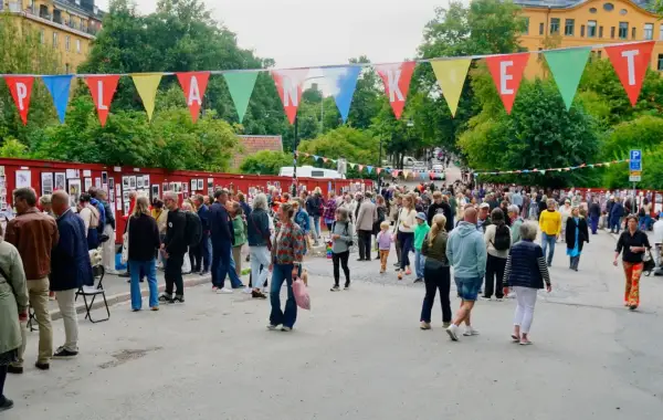 Färgglada vimplar med texten "Planket Stockholm" hänger över en livlig utomhusutställning med många besökare.