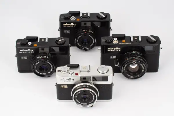 Fyra Minolta Hi-Matic kameror, varav en silverfärgad Minolta Hi-Matic F i förgrunden, omgivna av svarta modeller.