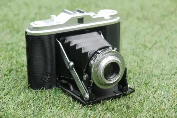 En klassisk Agfa Isolette hopfällbar kamera med läderdetaljer och en silverfärgad lins, placerad på grönt gräs.