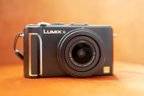 Svart kompaktkamera, en Lumix LX3 med Leica-objektiv, ligger på en orange yta.